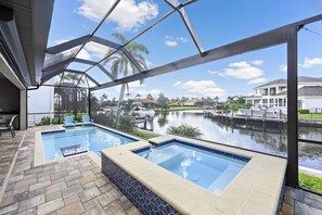 A swimming pool with two hot tubs, a covered patio, and a view of a canal with boats. - Waterfront Home | W Exposure, Pool & Spa (Marco Island)
