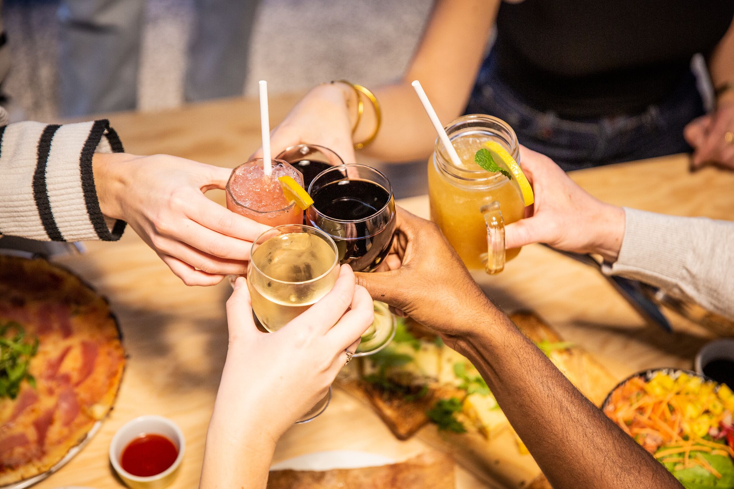 Un gruppo di persone brinda con bevande a un tavolo con pizza e insalata.