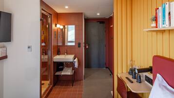 A modern bathroom with a sink, mirror, and towel rack. There is a shelf with books and a small plant.