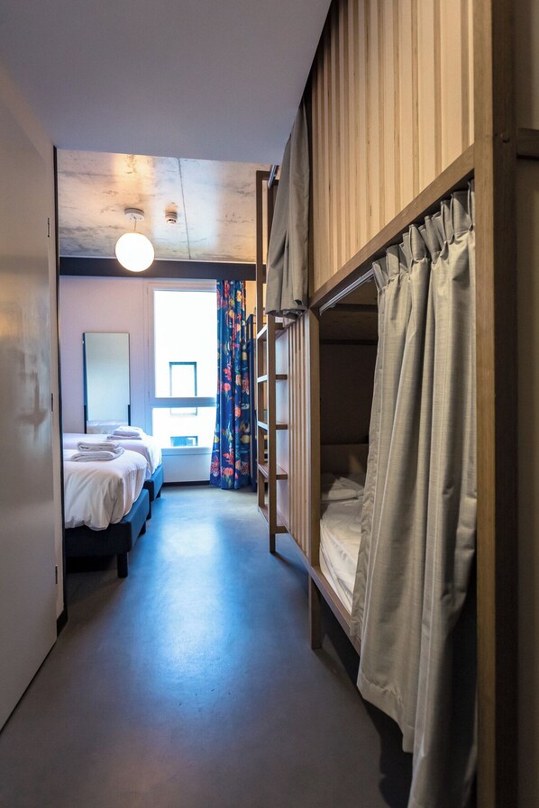 A room with bunk beds, a desk, a chair, and a window with curtains.
