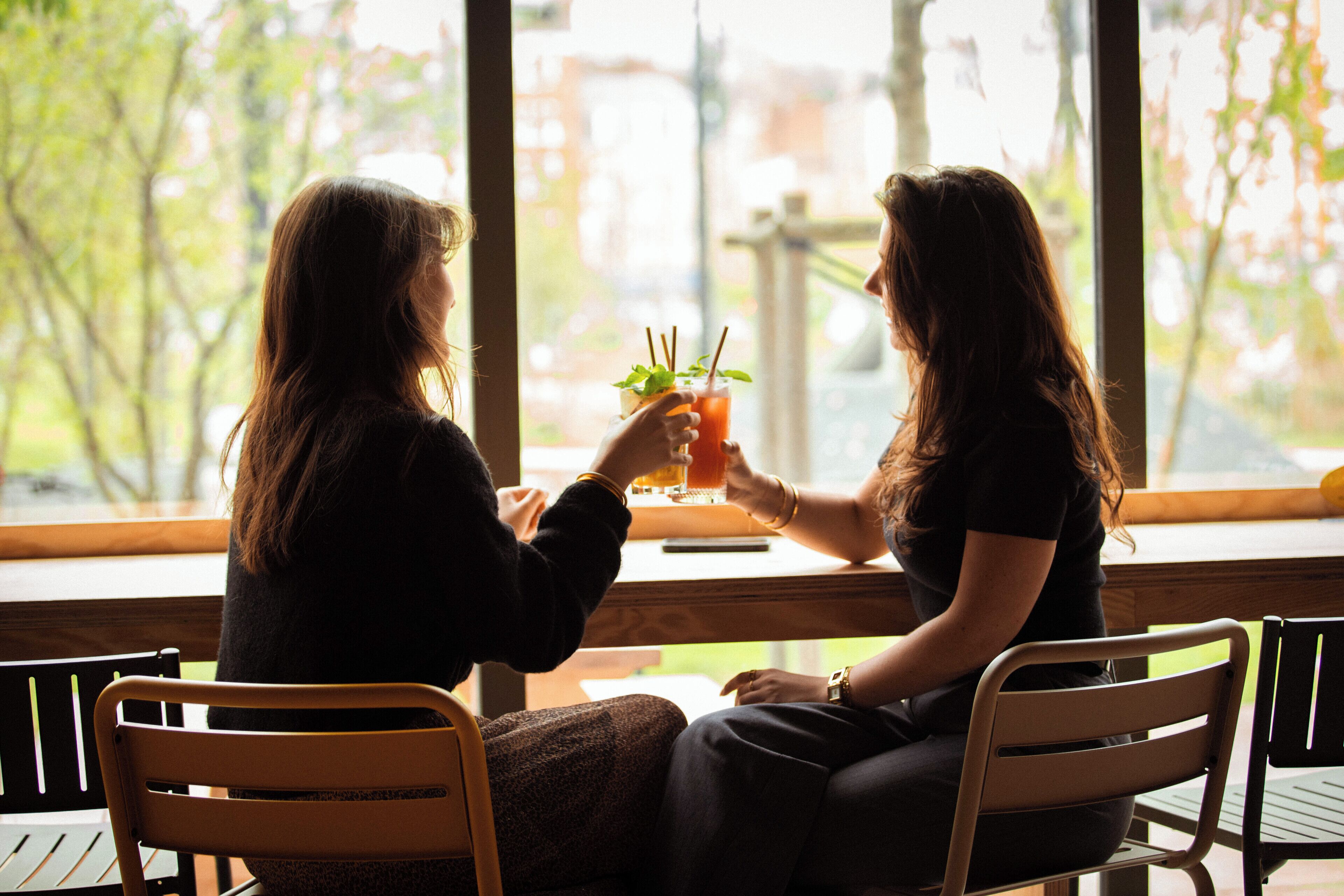 Two people sitting at a table by a window, holding drinks.