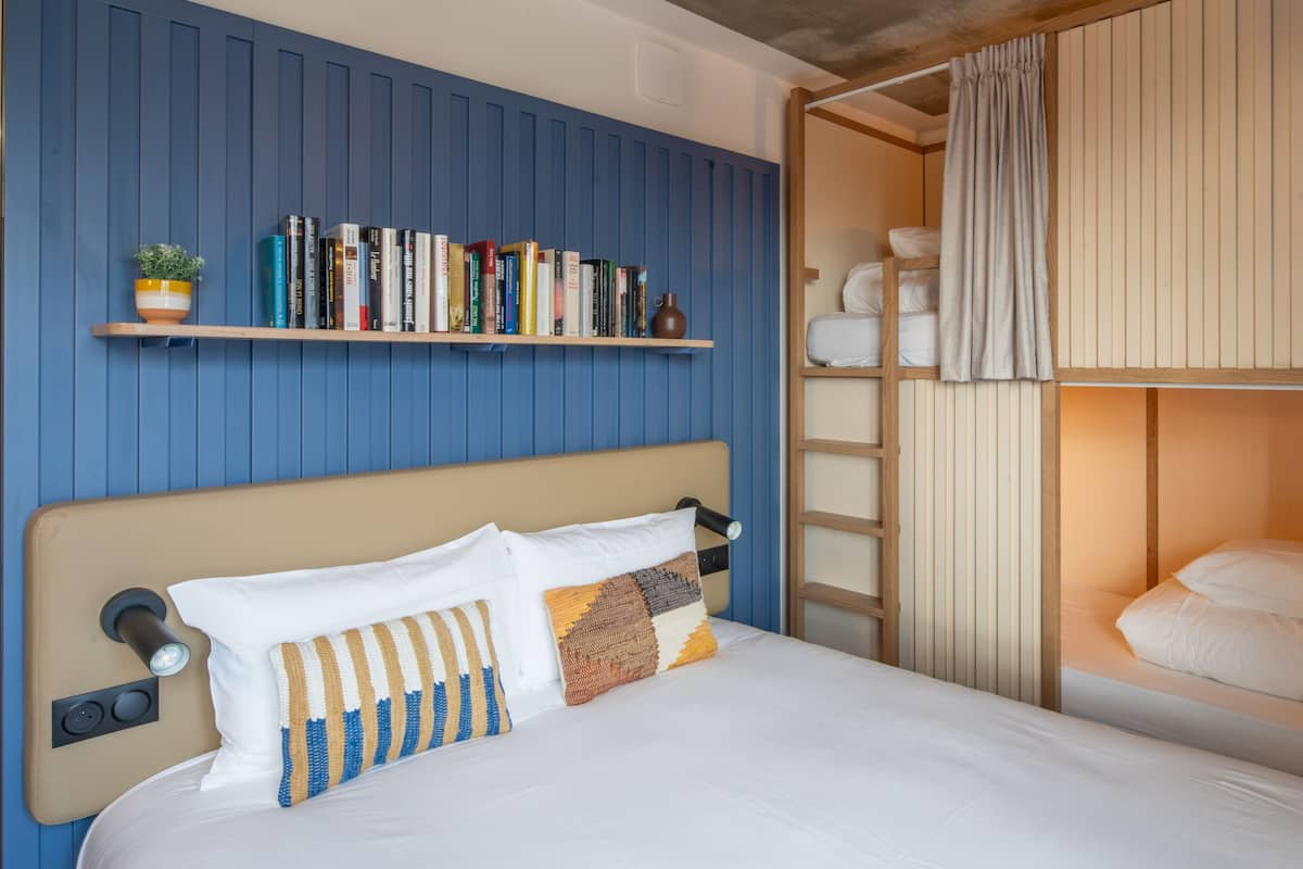 A bedroom with a bunk bed, a bookshelf with books, and a bedside table with a lamp.