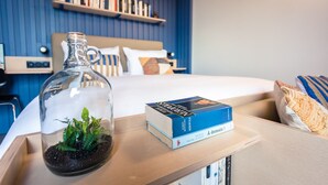 A neatly arranged hotel room with a bed, a bedside table with a book and a glass terrarium, and a shelf with books. - Jost Hotel Le Havre Gare (Le Havre)