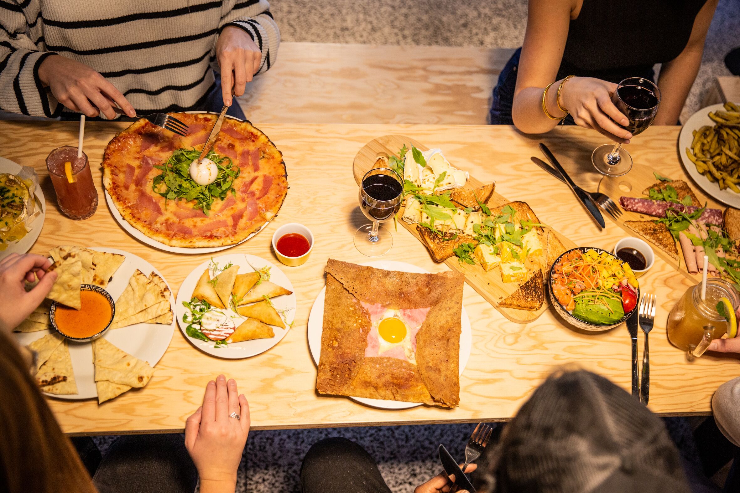 Un grupo de personas cenando en una mesa de madera con varios platos, como pizza, ensaladas y una bebida.