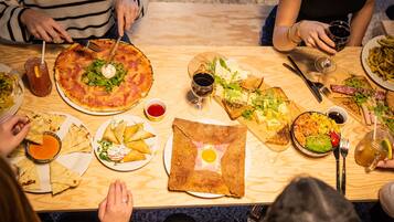 Un grupo de personas cenando en una mesa de madera con varios platos, como pizza, ensaladas y una bebida.