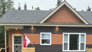 A modern house with a dark brown exterior, a wooden front door, two windows, and a picnic table in the front yard.