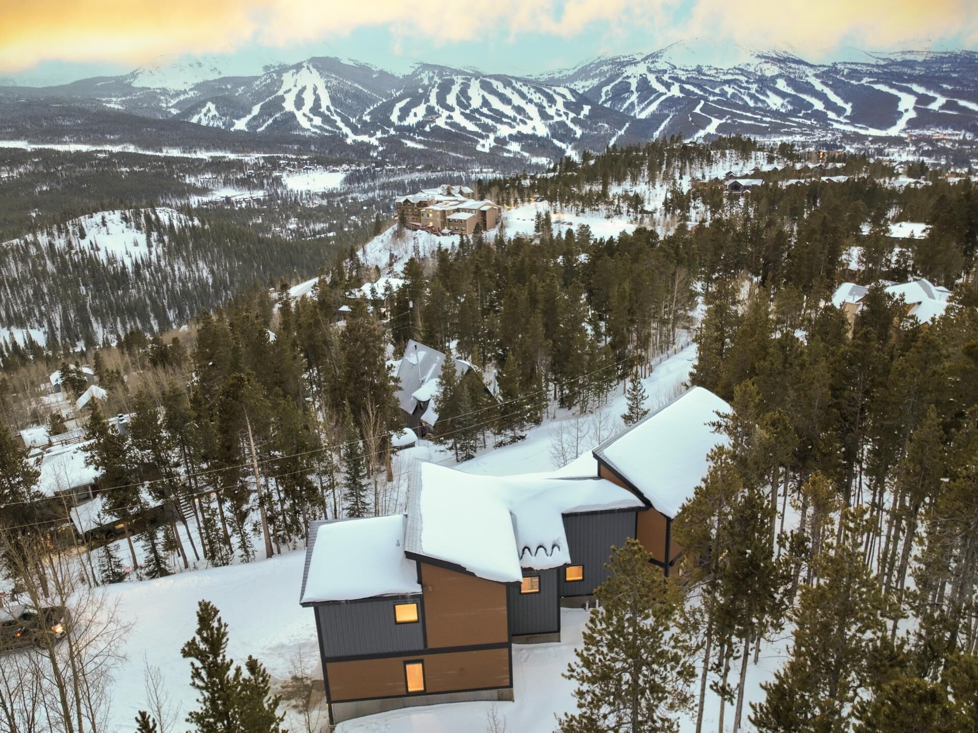 Eine moderne Lodge mit mehreren Holzhütten, umgeben von schneebedeckten Wäldern und Bergen.