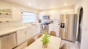 A modern kitchen with white cabinetry, stainless steel appliances, and a dining table with chairs. - Mega Group Block: 4 Units | Sleeps 10-16 (Deerfield Beach)
