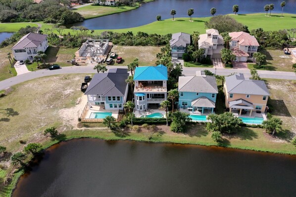 An aerial view of a residential area with houses, a swimming pool, and a body of water.