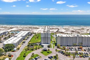 A coastal hotel with multiple buildings, a parking lot, and a beach in the background.