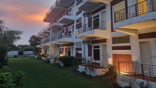 A multi-story hotel with balconies, a well-maintained lawn, and a clear sky. - Yoga Rishi (Narendranagar)