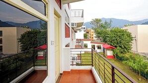 A residential building with a balcony, a view of the surrounding neighborhood, and mountains in the background. - Yoga Rishi (Narendranagar)