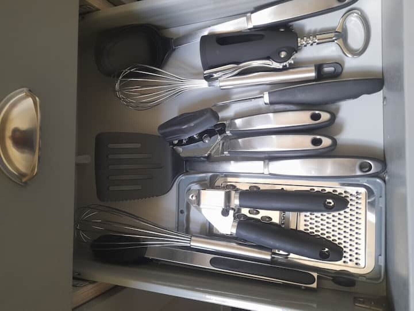 A kitchen drawer with various utensils including a whisk, spatula, and grater.
