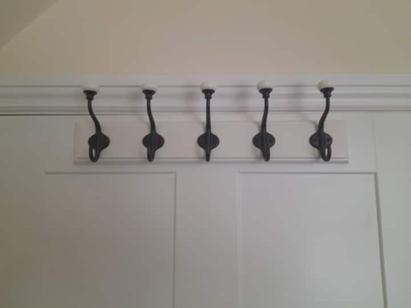 A white door with five black wall-mounted hooks.