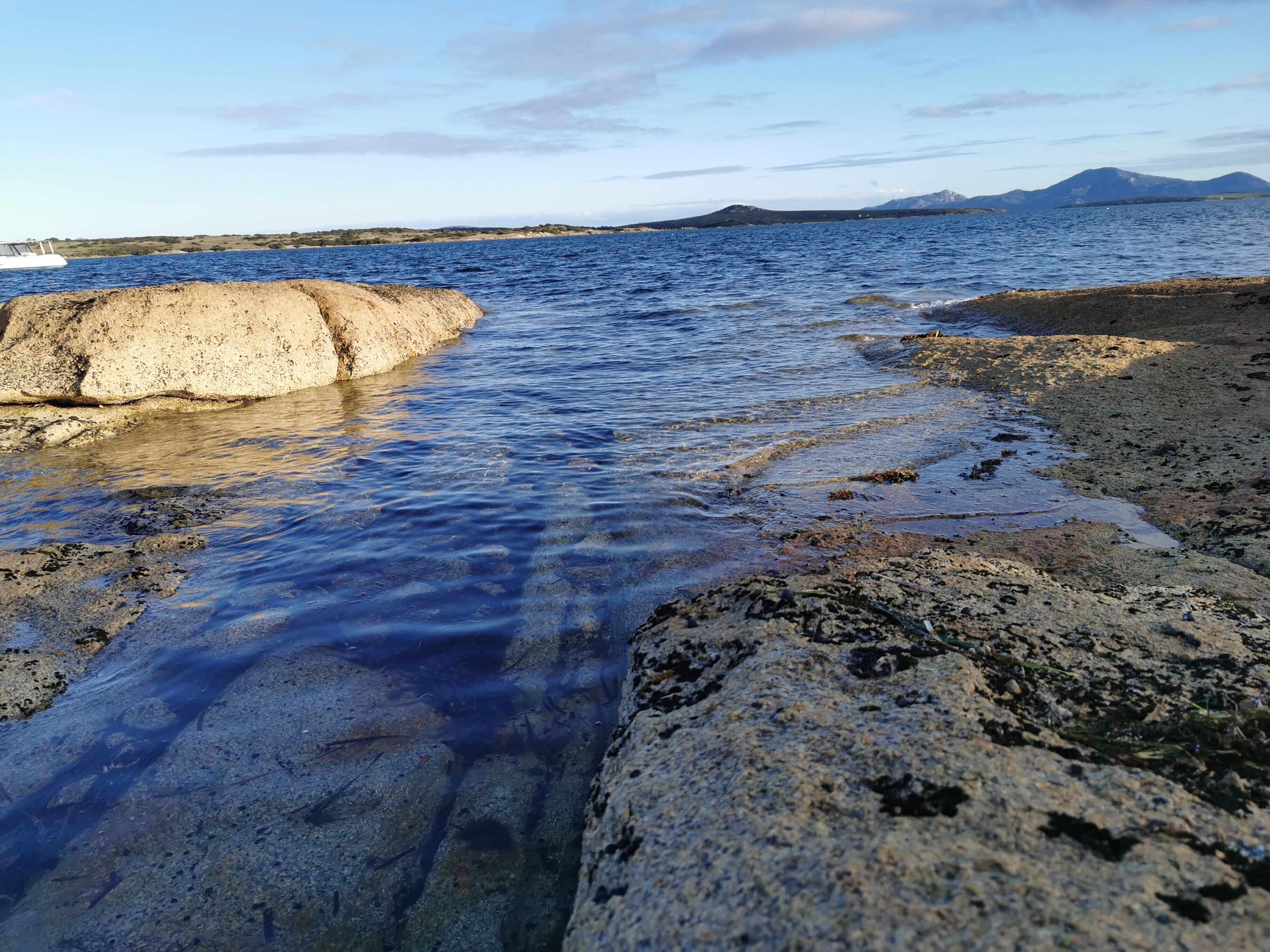 Una costa rocosa amb aigua cristal·lina i muntanyes a la distància.