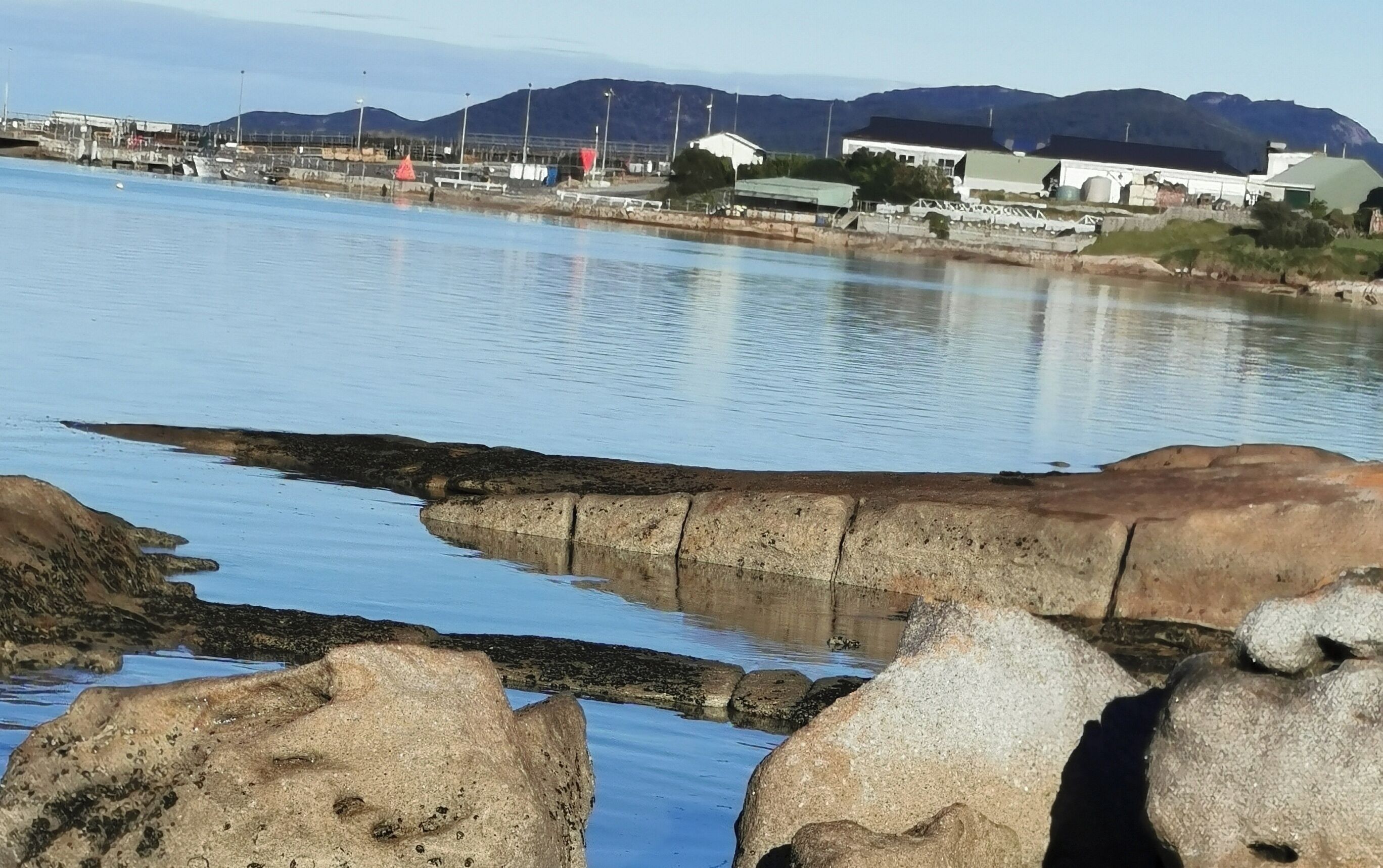 A coastal view with rocky shores, calm water, and distant buildings.