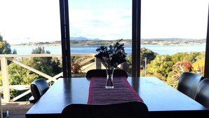 A dining table with a vase of flowers, two chairs, and a view of a lake and mountains through large windows.
