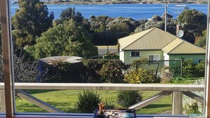 A dining area with a view of a coastal landscape, including a house and trees.
