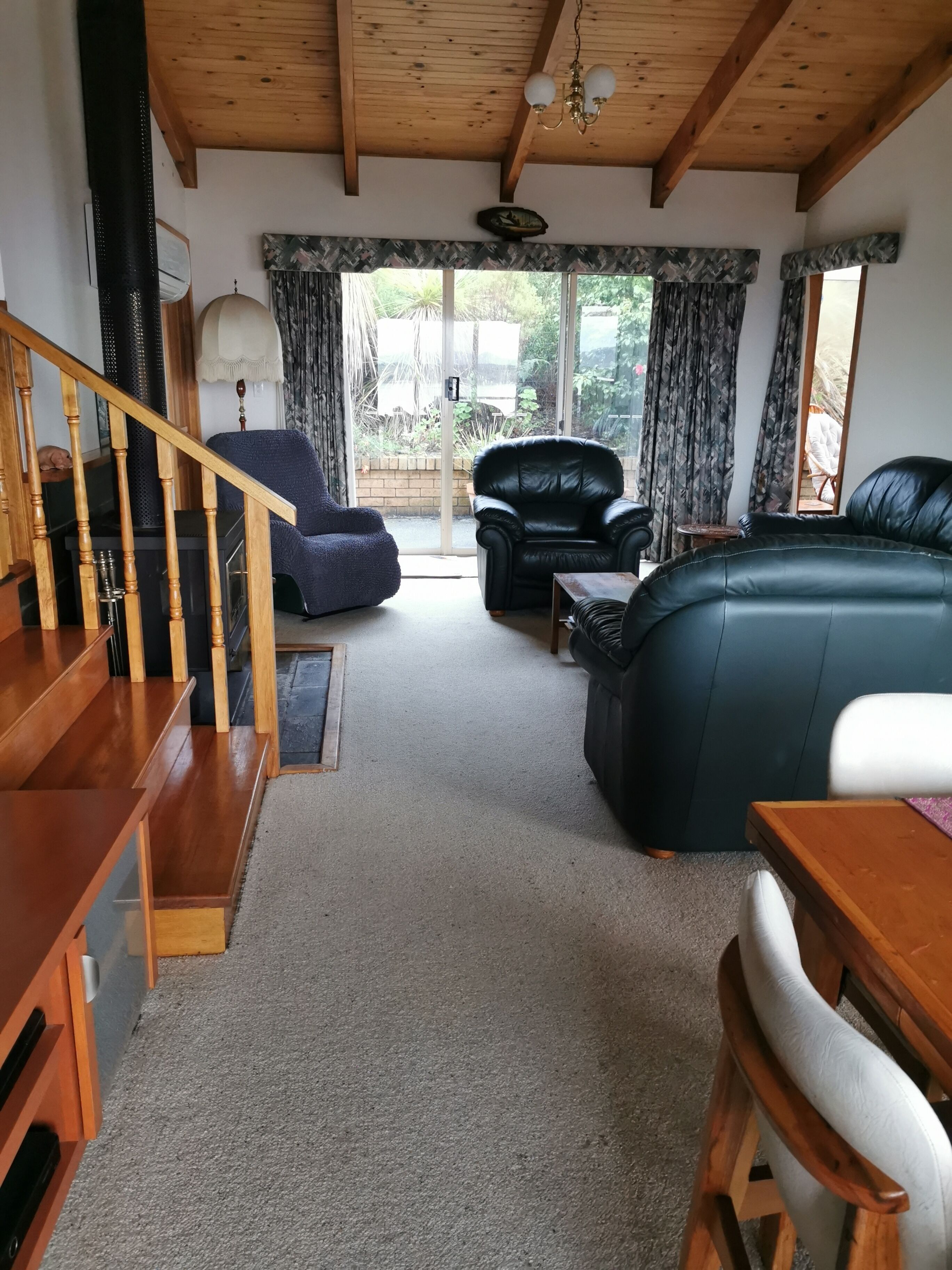 A cozy living room with a wooden staircase, a black leather sofa, a blue armchair, and a dining table.