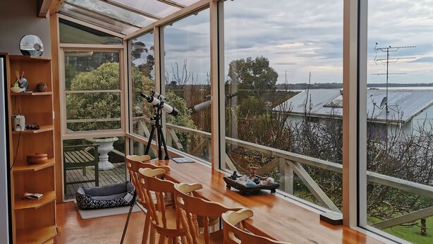 A spacious room with a large glass window, wooden furniture, and a telescope on a tripod.