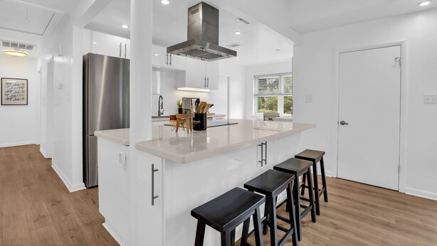 Una cocina moderna con armarios blancos, un refrigerador de acero inoxidable y una isla central con taburetes de bar.