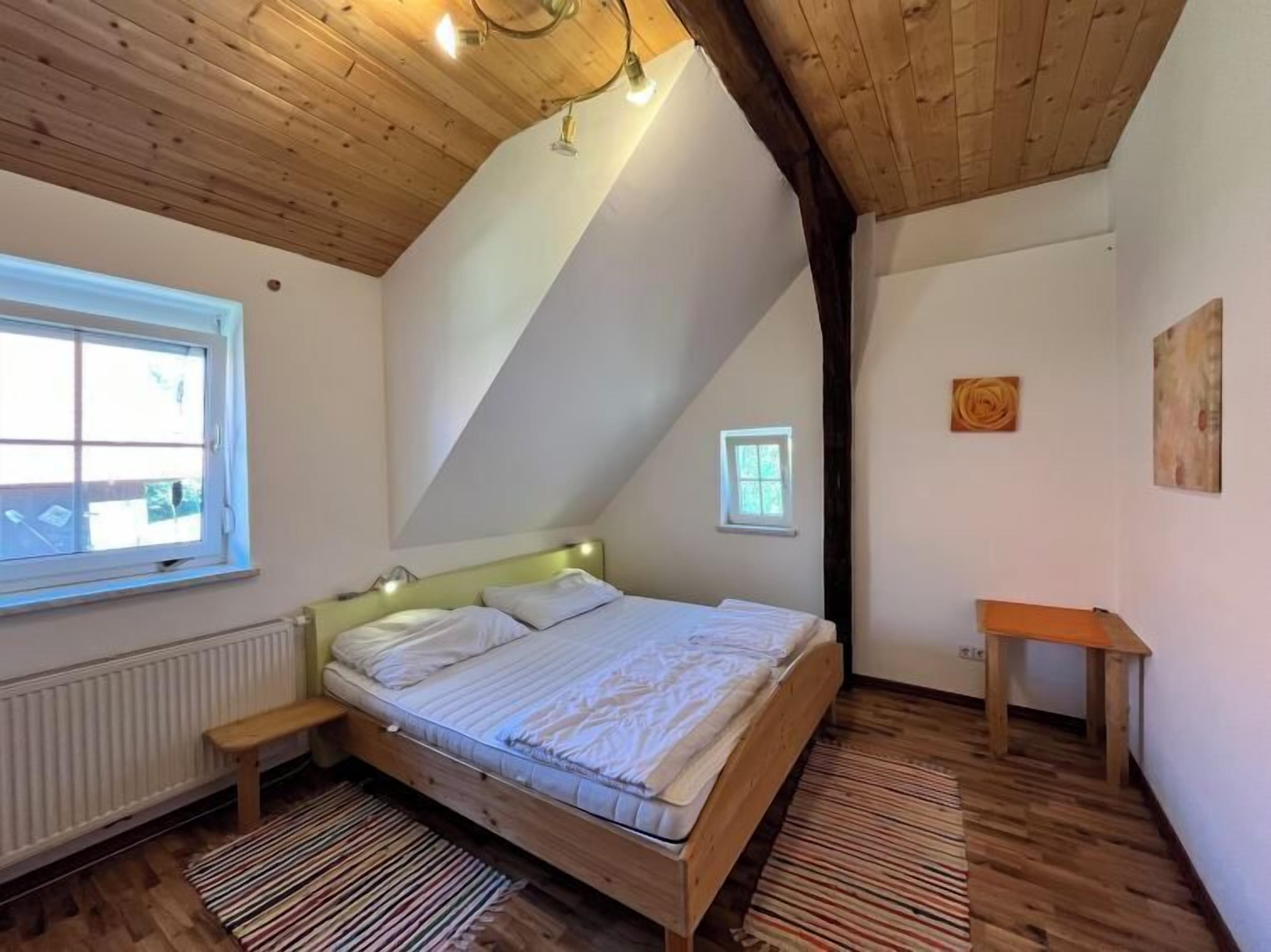 A bedroom with a sloped ceiling, a bed, a small table, and a window.