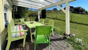 Une terrasse extérieure avec une table et des chaises, un espace abrité et une vue sur un paysage verdoyant.