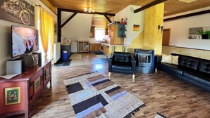 Un vaste espace de vie doté d’un plafond en bois, d’un téléviseur, d’un canapé, d’une cheminée et d’une cuisine à l’arrière-plan.