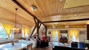 Une pièce spacieuse dotée de planchers en bois et d’un plafond haut, comprenant un coin repas avec une table et des chaises, un canapé et un téléviseur.