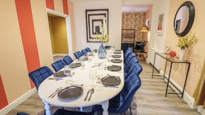 A dining area with a long table set for a meal, blue upholstered chairs, and a vase with flowers. - Carlton House (Skegness)