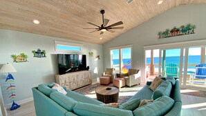 Ein geräumiges Wohnzimmer mit einem großen, türkisblauen Sofa, einer Holz-Unterhaltungseinrichtung und einem Deckenventilator.