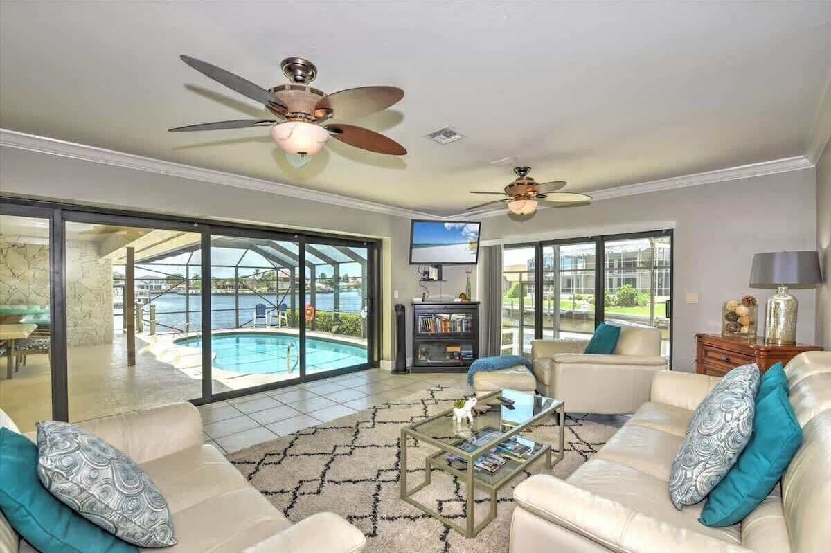 A spacious living room with a large glass door leading to a pool, ceiling fans, a television, and a bookshelf.