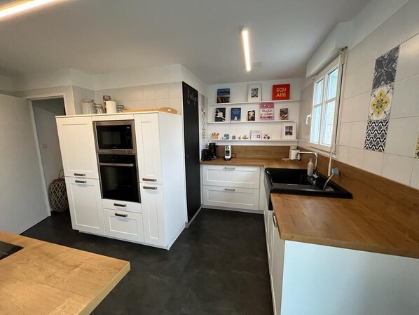 A compact kitchen with white cabinetry, a microwave, a coffee machine, and a wooden countertop. - Fisherman's house / Penty in Plogoff with terrace, garden and sea view near the beach (Plogoff)