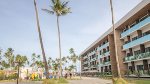 A hotel with multiple balconies, palm trees, and a central plaza with seating areas. - Maceió Mar Resort All Inclusive (Maceió)