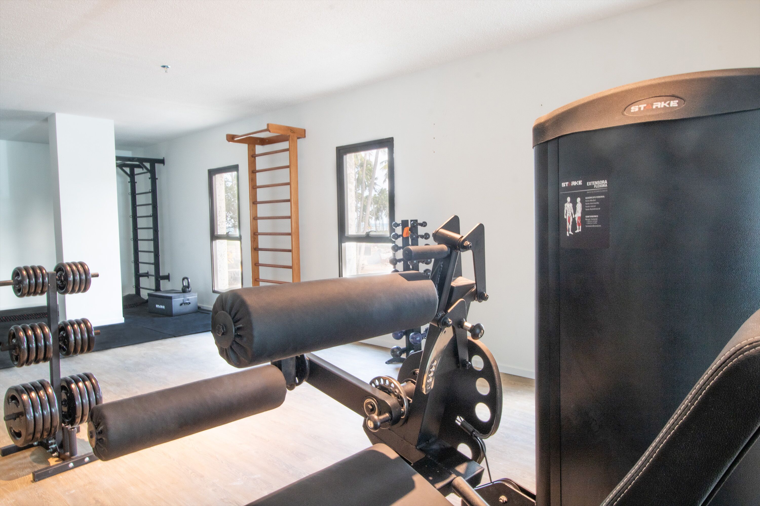 Uma academia com equipamentos de musculação, barra de exercícios e suporte fixado na parede.