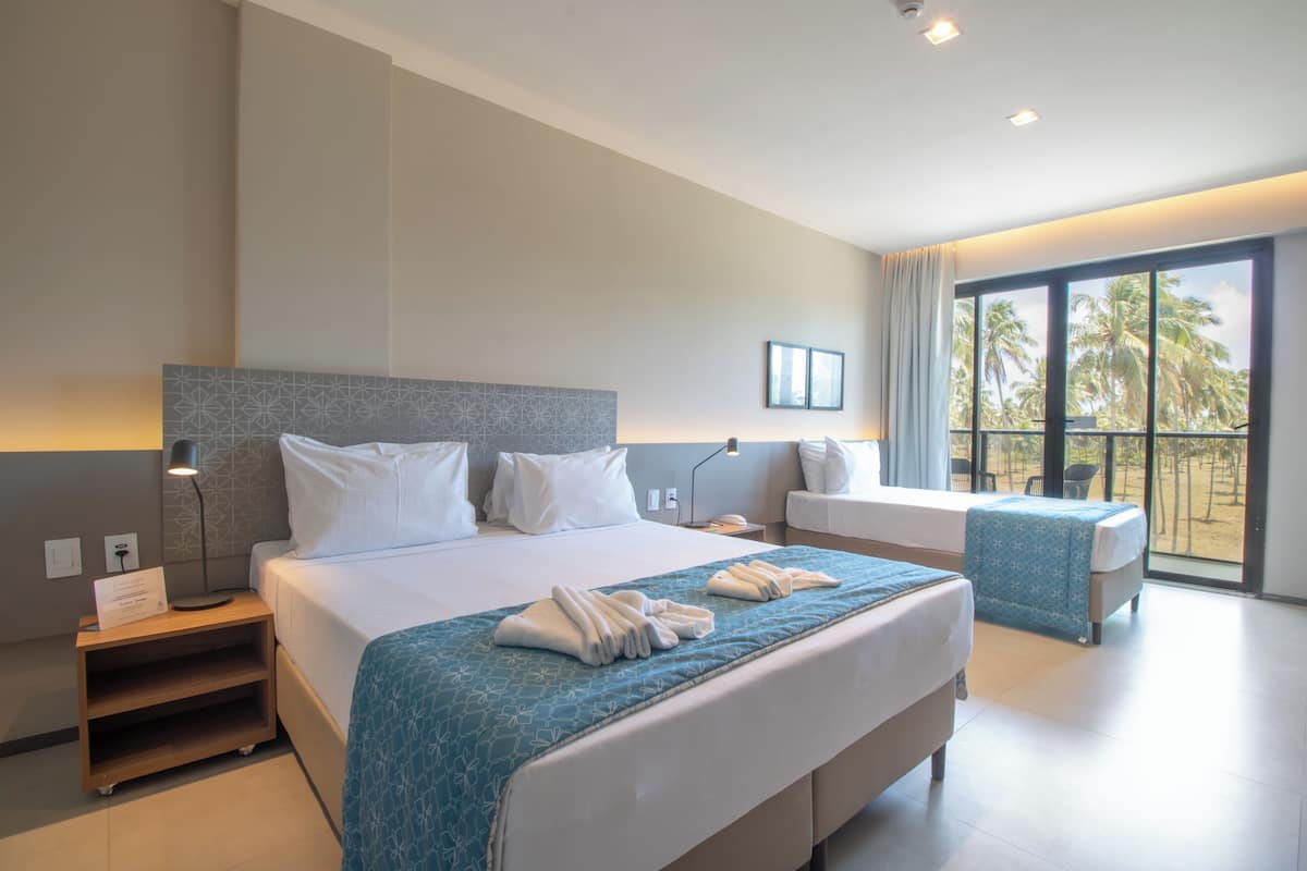Habitación de hotel moderna con una cama grande, una mesita de noche, un escritorio y vistas a palmeras a través del ventanal.