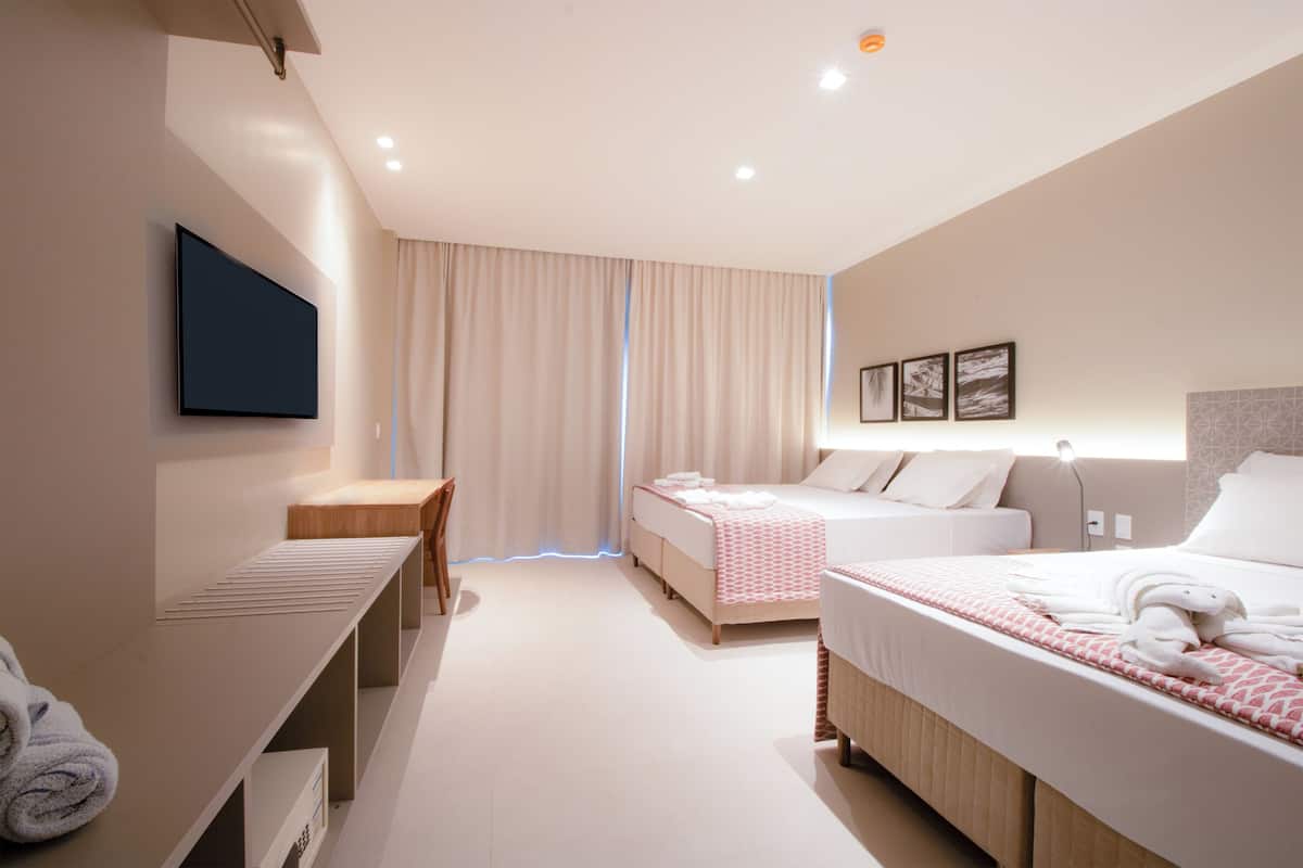 Habitación de hotel moderna con una cama grande, otra más pequeña, un escritorio y un televisor montado en la pared.