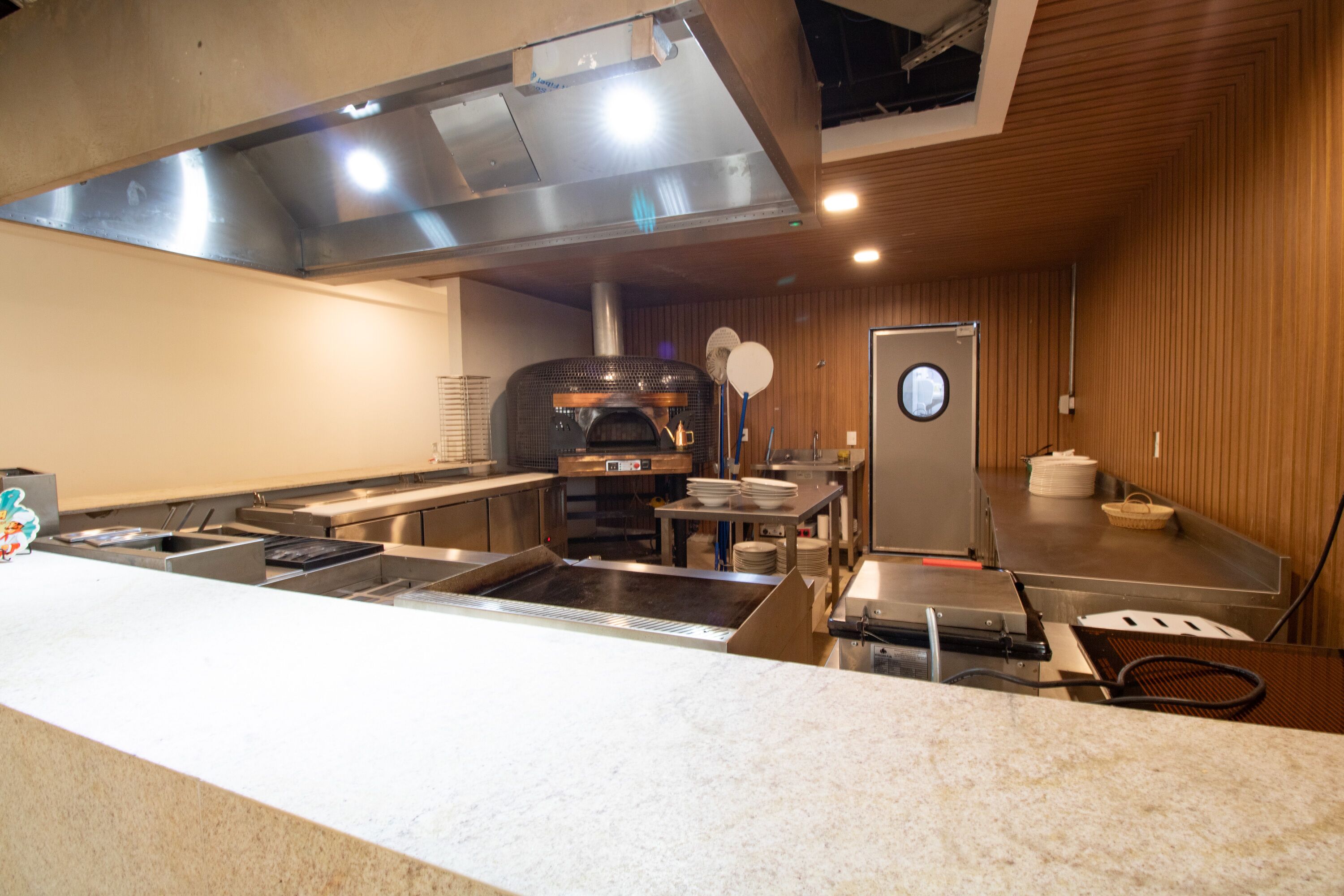Una cocina comercial con electrodomésticos de acero inoxidable, un revestimiento de madera y un horno para pizzas.