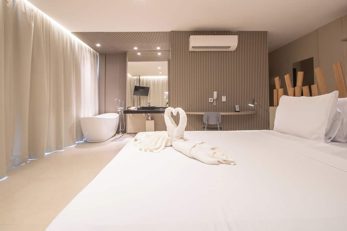 Una habitación de hotel moderna con una cama grande, un baño con bañera, un tocador con espejo y un televisor de pantalla plana.