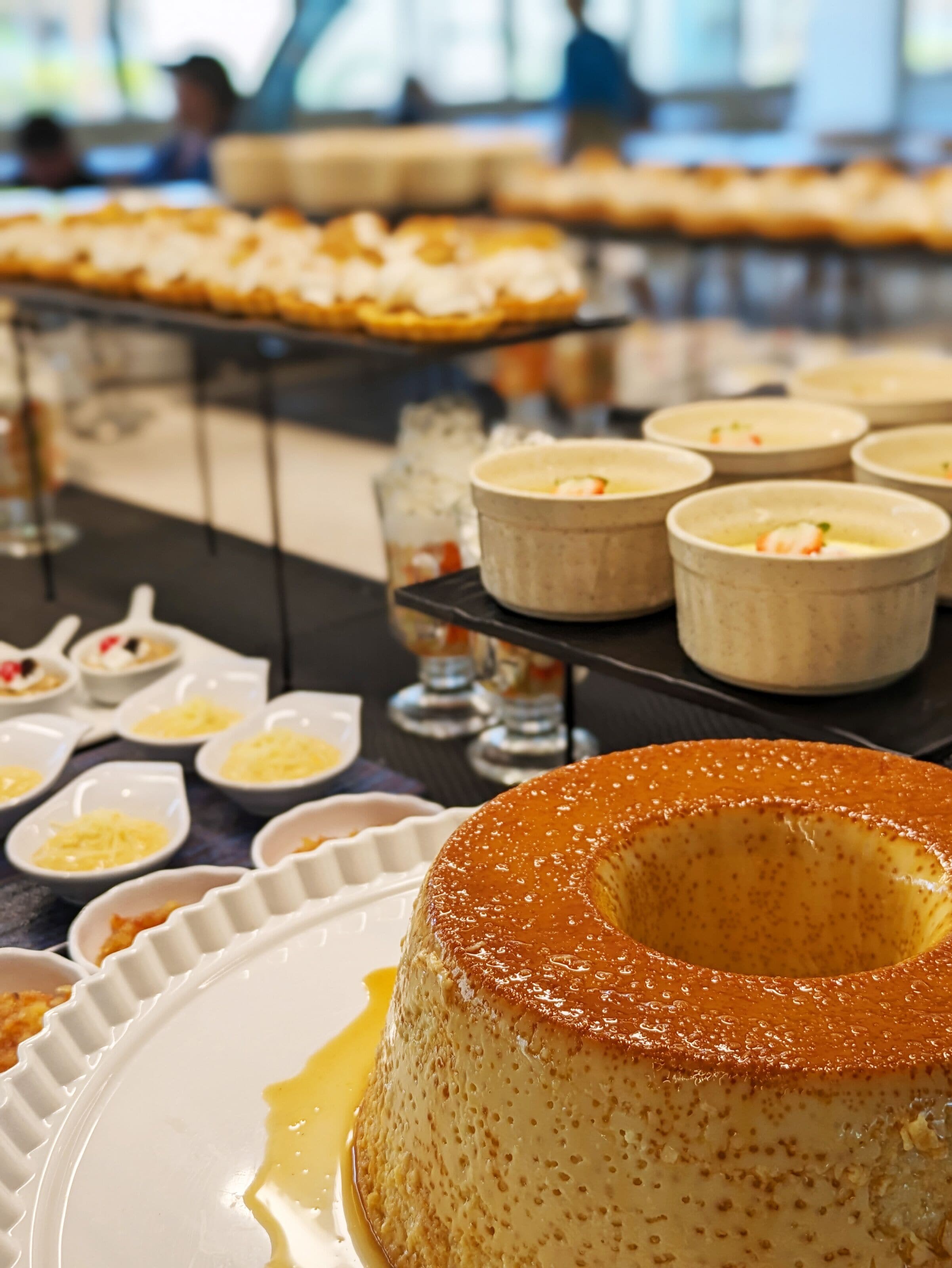 A dessert display with a caramel flan in the foreground and various other desserts in the background.