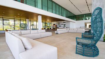 A spacious lobby with a large white sectional sofa, a unique blue woven chair, and a high ceiling with large windows.