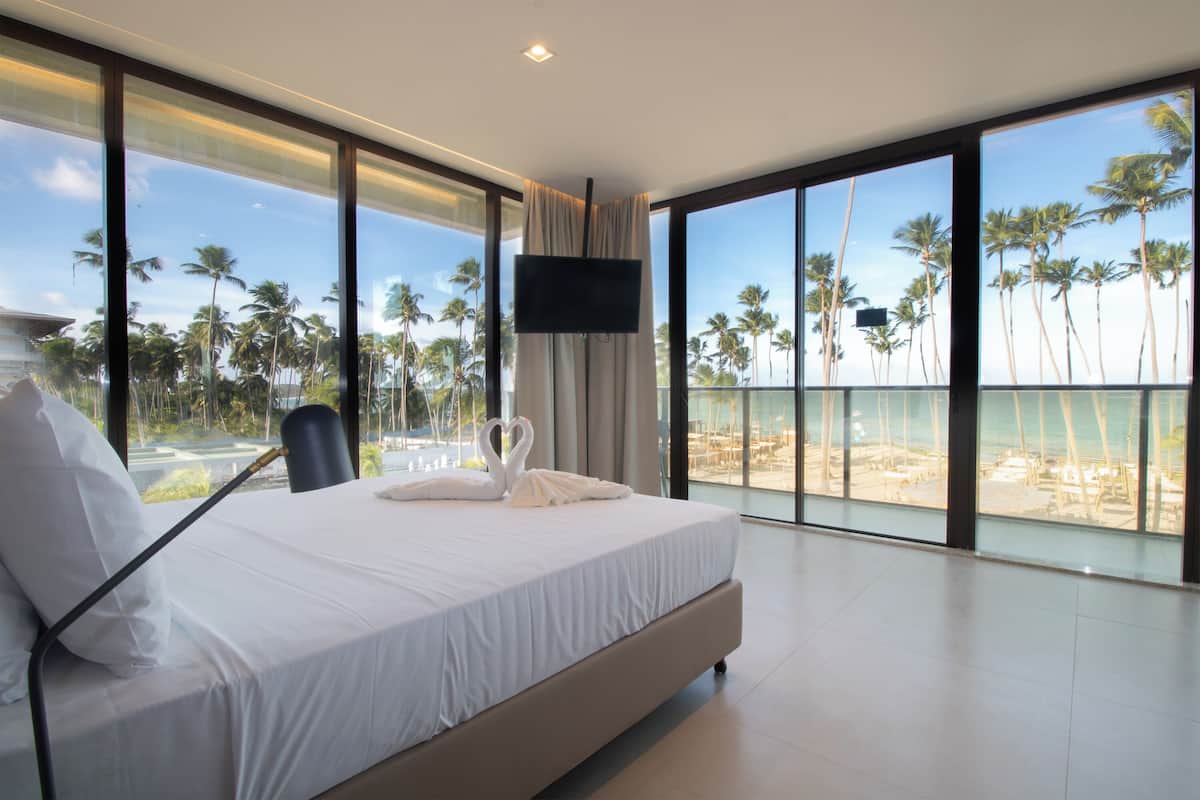 Una habitación de hotel moderna con una cama grande, un televisor de pantalla plana y un balcón con vistas a palmeras y la playa.