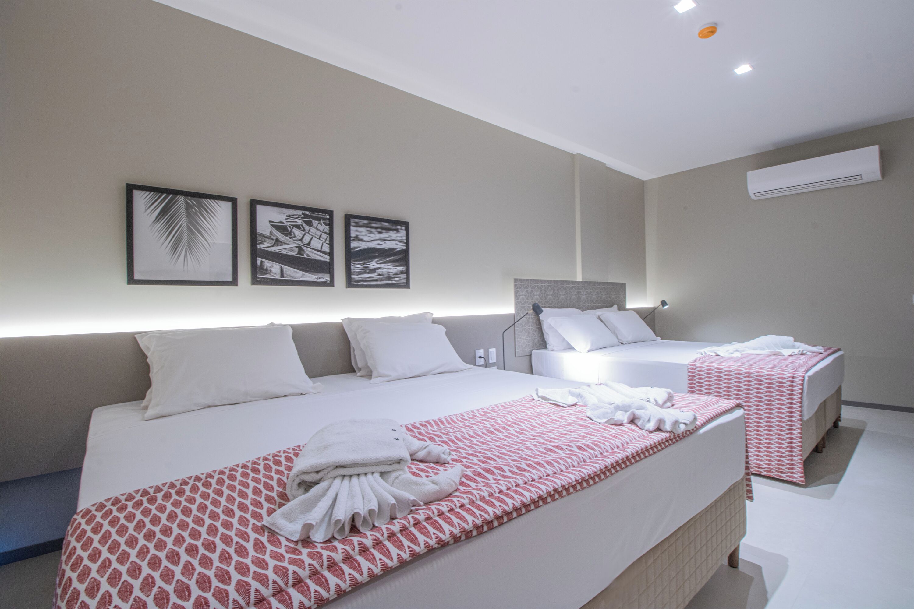 Habitación de hotel con una cama grande, una cama más pequeña y un sofá. Hay tres cuadros en la pared.