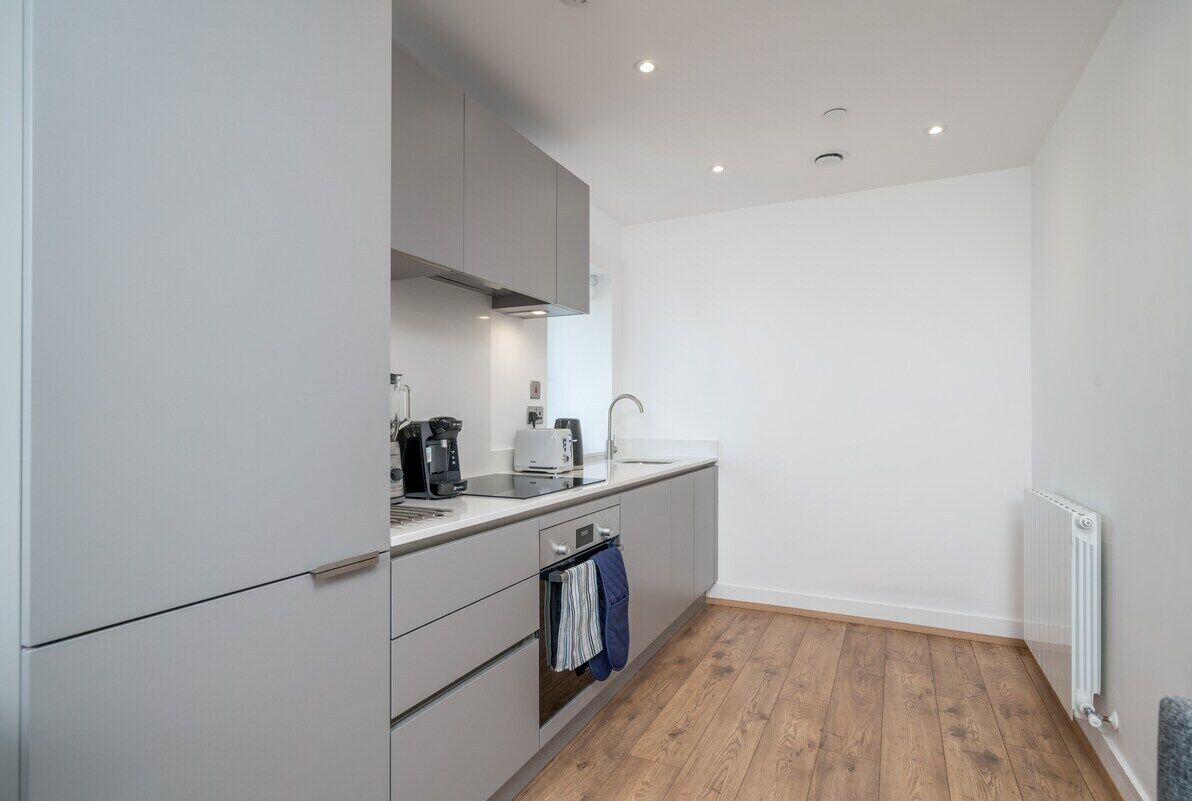 A modern kitchen with grey cabinets, a built-in oven, a sink, and a coffee maker.