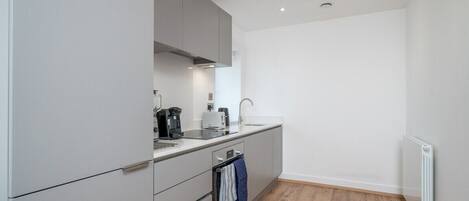 A modern kitchen with grey cabinets, a built-in oven, a sink, and a coffee maker.
