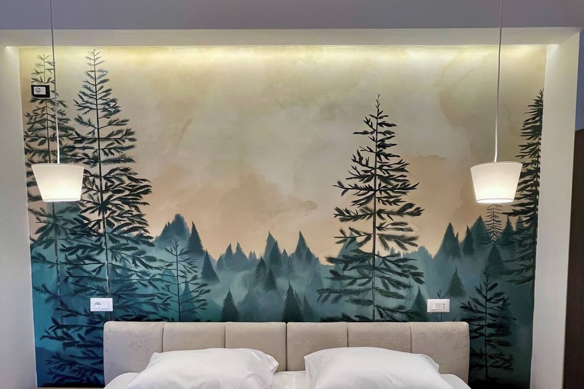 A hotel room with a bed, two nightstands, a headboard with a forest mural, and two pendant lights.