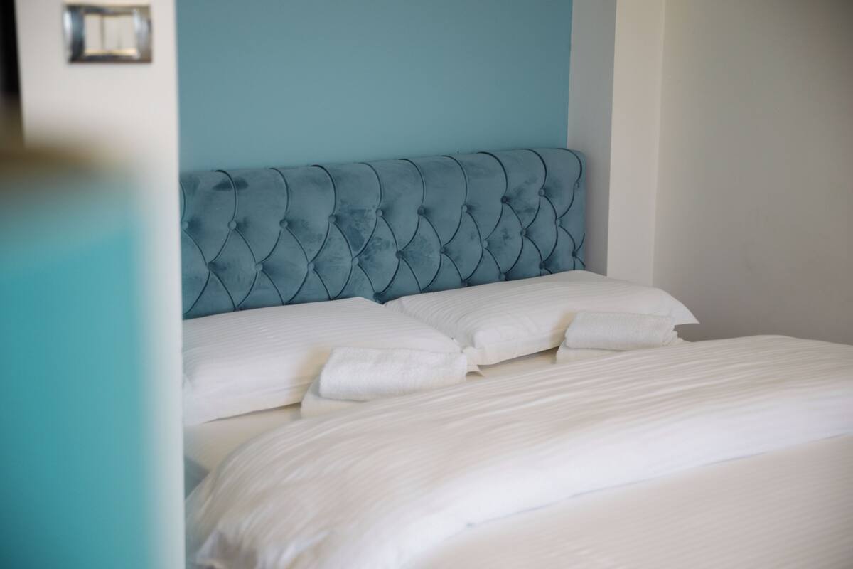 A bed with a tufted headboard, white bedding, and a teal wall.