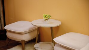 Una habitación con dos sillas blancas acolchadas, una mesita redonda con una planta y una alfombra mullida de color blanco.