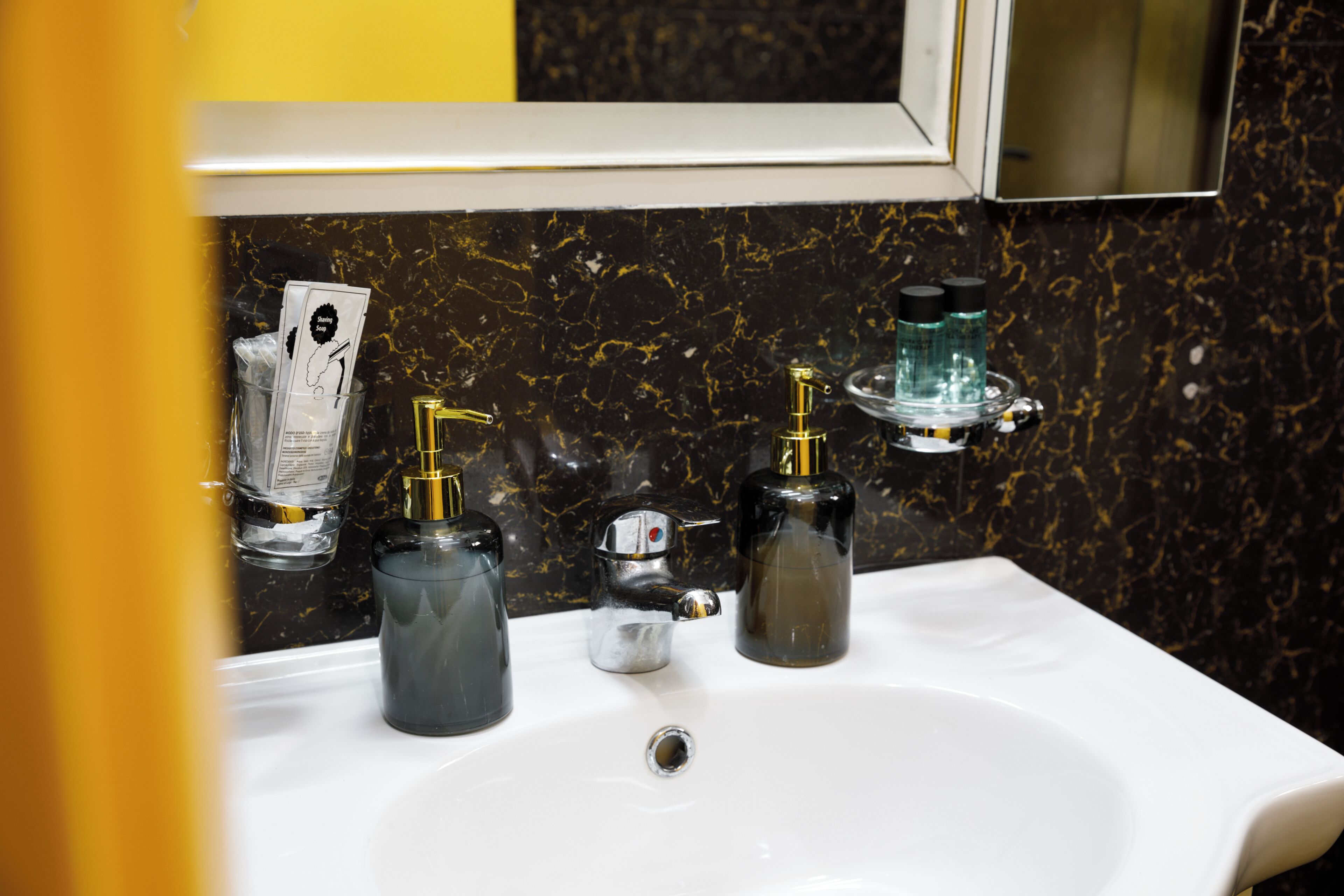 Un bany amb un lavabo blanc, tres dosificadors i un mirall a la part superior.