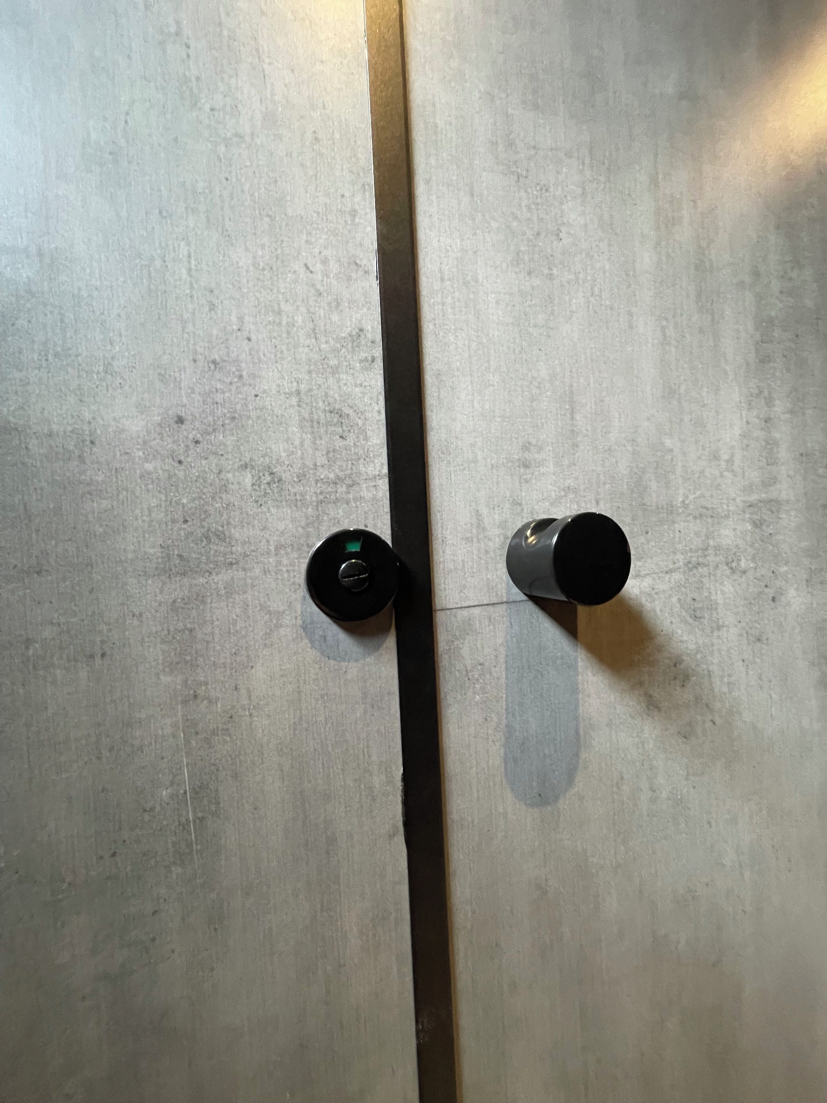 Eine Tür mit einer vertikalen Metallstange, zwei runden Türgriffen und einer strukturierten Oberfläche.